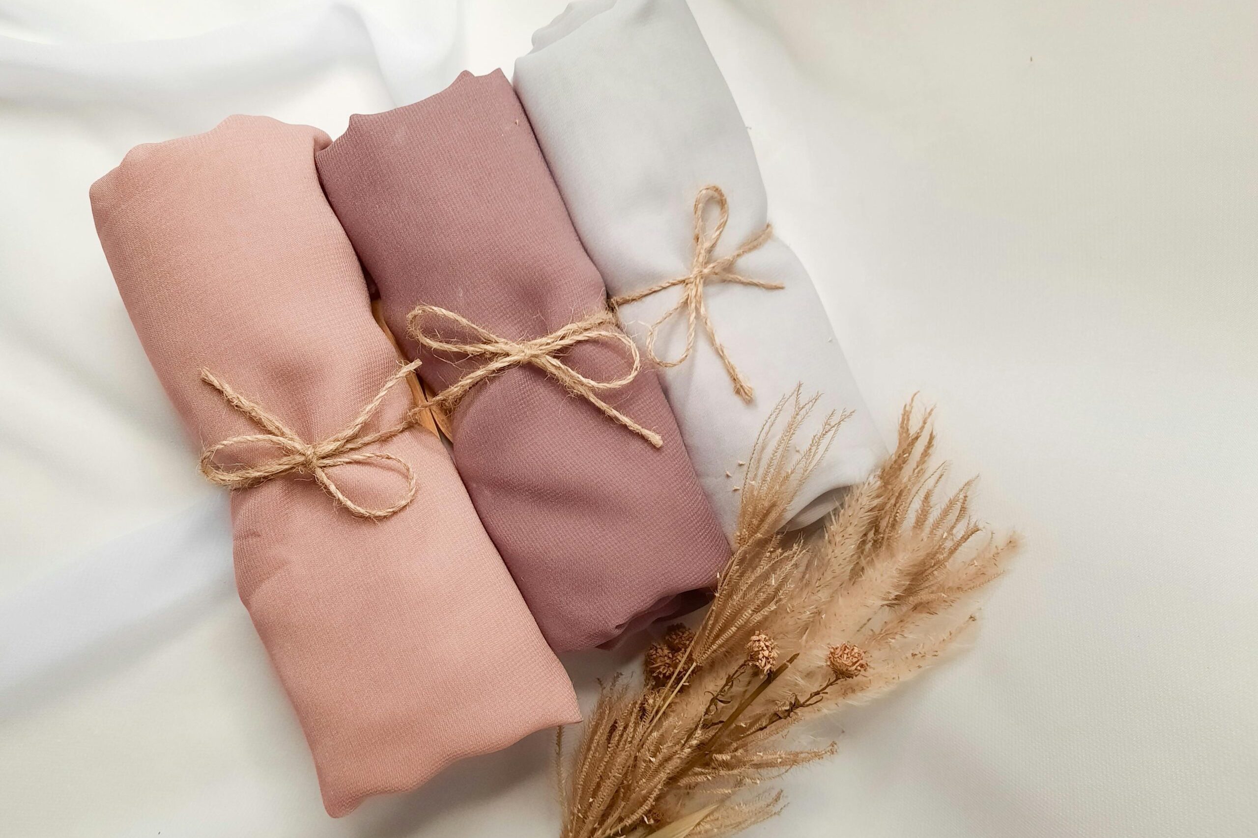 Close-up of rolled fabric in soft pink, taupe, and white shades tied with twine, featuring dried flowers.